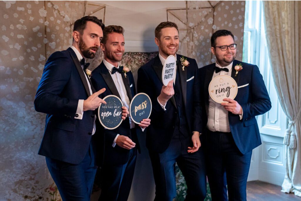 Groomsmen using a wedding photo booth with props